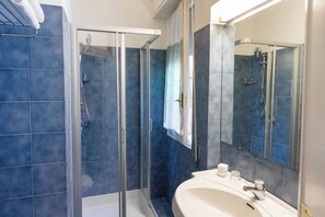 A modern bathroom with a glass-enclosed shower, a white sink, and a large mirror. - Cav Approdo (Castiglione della Pescaia)