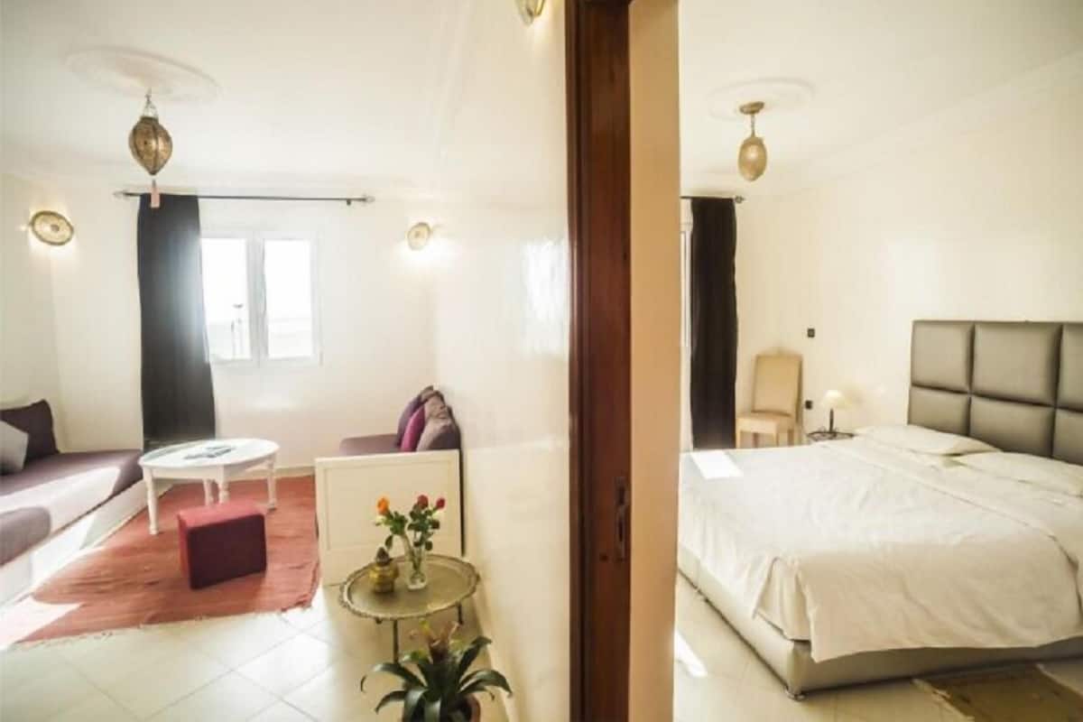 A hotel room with a bed, a sofa, a small table with a vase, and a window.