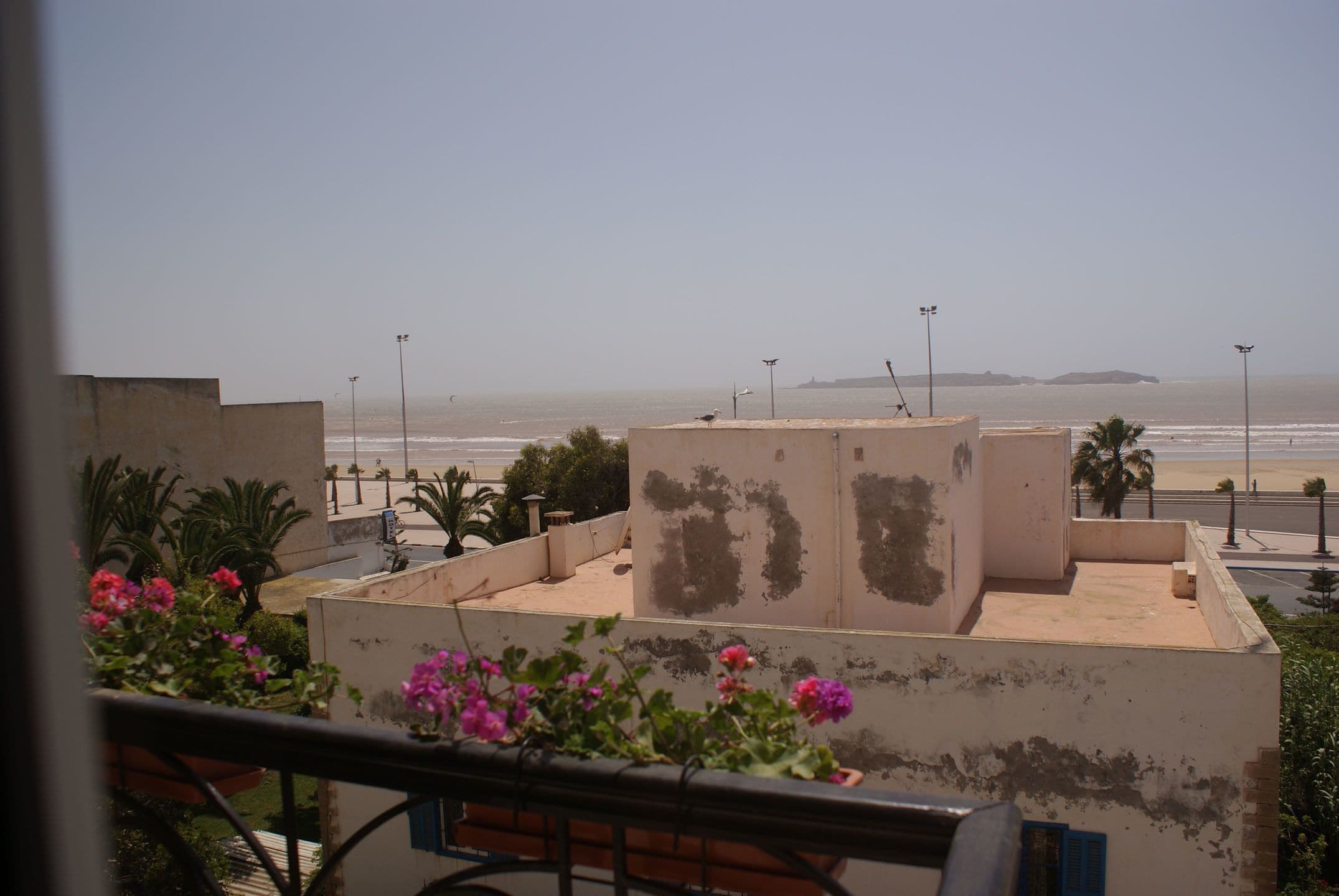 A balcony with a view of the beach, a concrete structure, and some potted plants.
