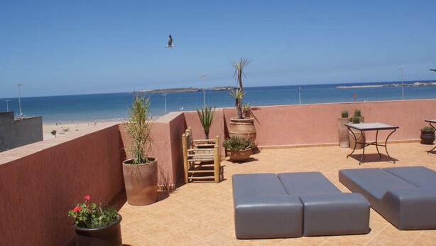 Terraza en la azotea con vista a la playa, plantas en macetas y mobiliario de exterior.