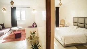 Habitación de hotel con cama, sofá, una mesita con un jarrón y ventana con cortinas.