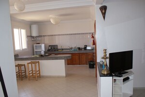 Una cucina con isola centrale, sgabelli di legno, televisore e macchina da caffè.