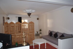 Una sala de estar con un sofá, un televisor, un separador decorativo y un ventilador de techo.