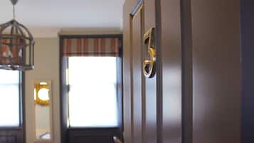 Eine Tür mit Messingklinke und Schlüsselloch, ein Fenster mit gestreifter Vorhang und eine hängende Leuchte.