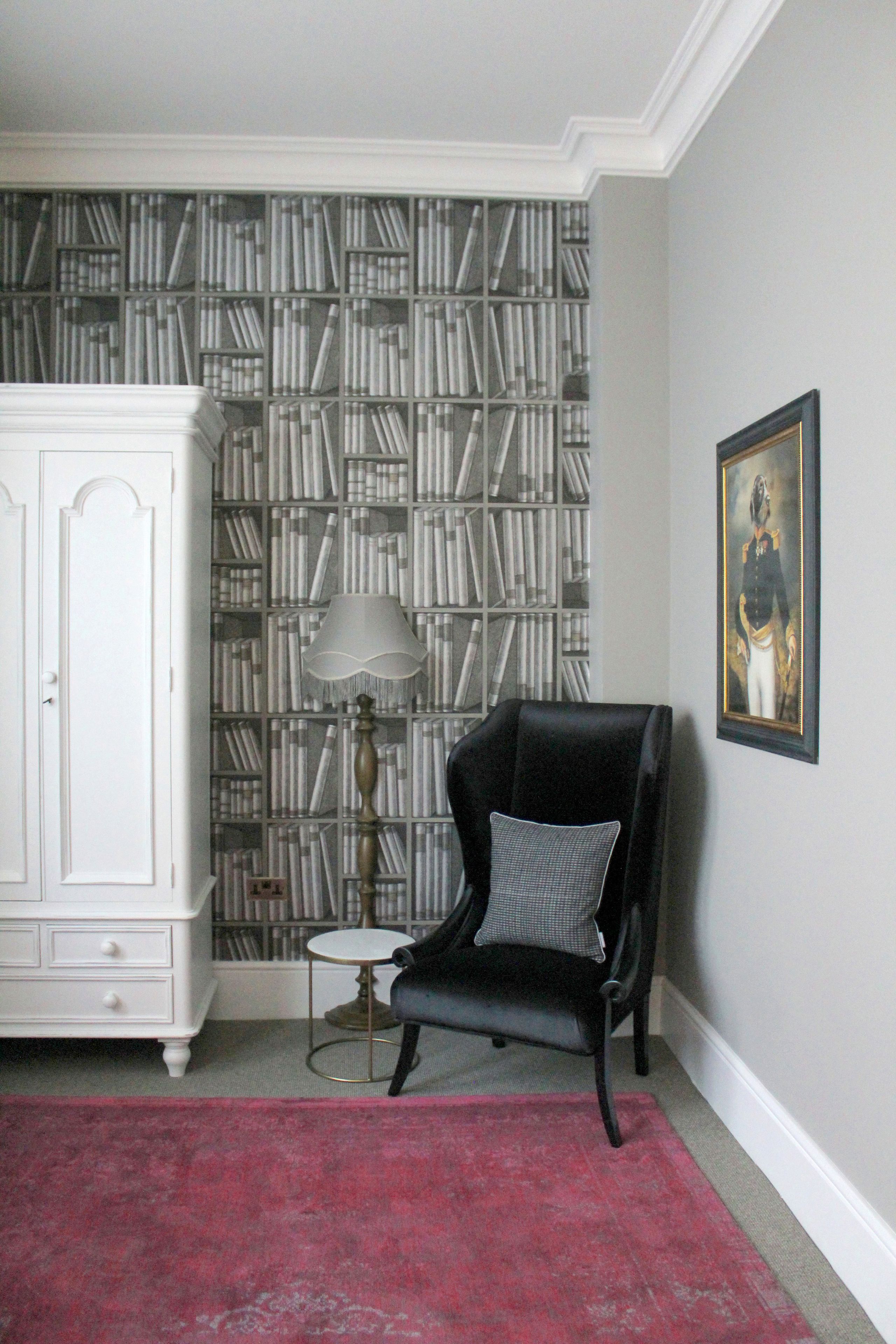 A room with a bookshelf, a black armchair, a small round table, and a framed picture on the wall.