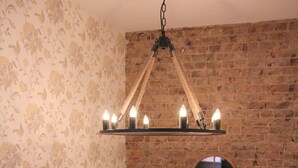 A room with a brick wall, a decorative mirror, and a hanging light fixture with candles. - The One Tun Pub and Rooms (London)