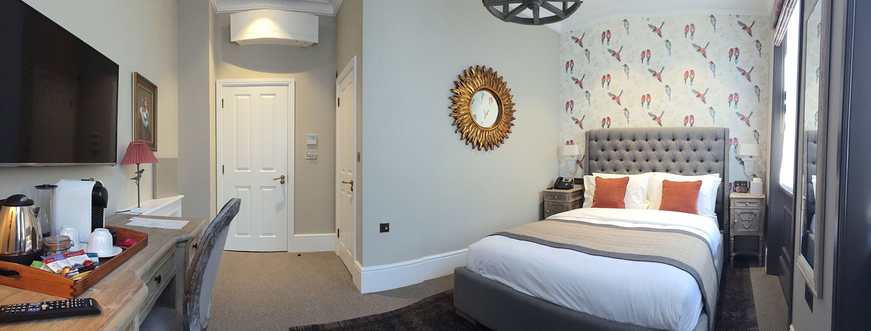A hotel room with a large bed, a desk with a chair, a TV, and a wall with a bird pattern.