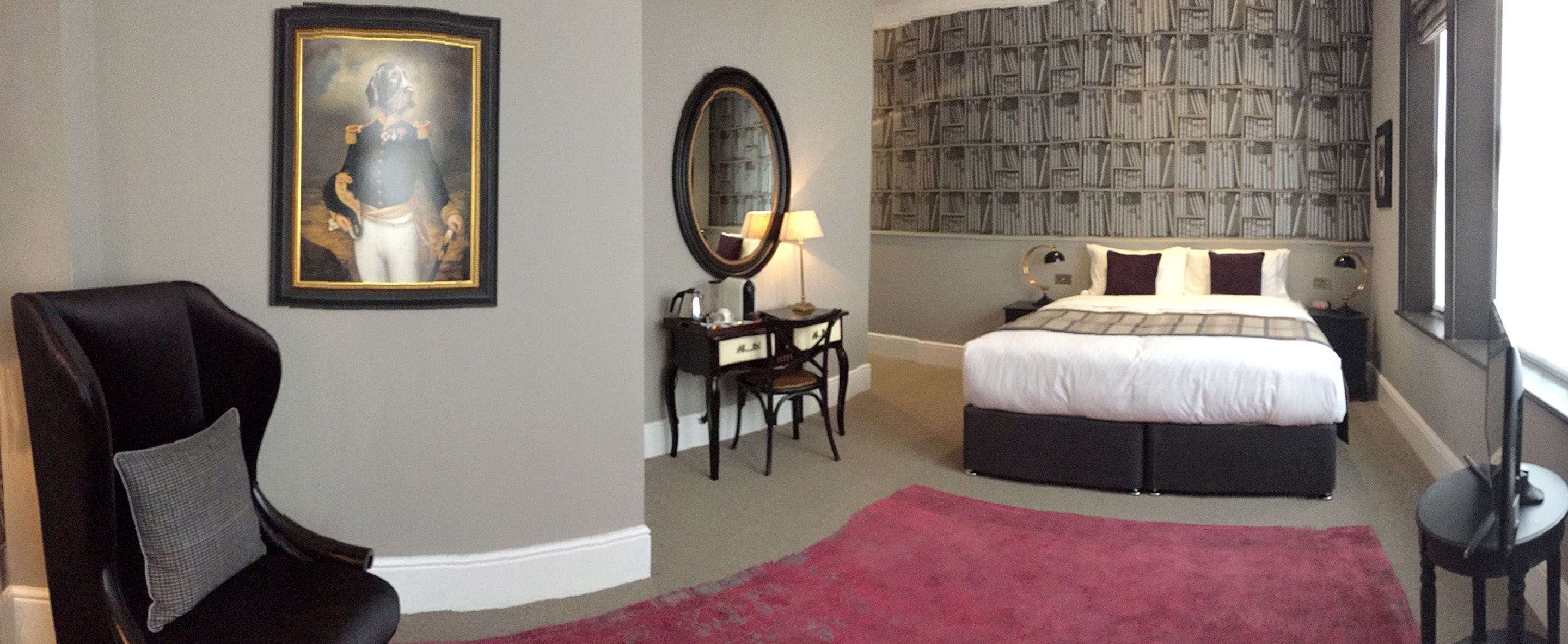 Habitación de hotel con una cama, un escritorio, una silla, un espejo grande y un cuadro en la pared.