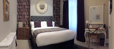 A bedroom with a large bed, a desk, a chair, a bookshelf, and a mirror.