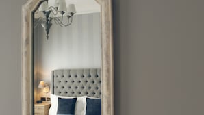 A bedroom with a tufted headboard, a bed with white and dark blue bedding, and a nightstand with a lamp. - The One Tun Pub and Rooms (London)