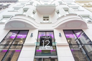 Η πρόσοψη του ξενοδοχείου Twave 12 Revay διακρίνεται για τον μοντέρνο αρχιτεκτονικό σχεδιασμό της, με μεγάλα παράθυρα και μια επιβλητική επιγραφή στην είσοδο.