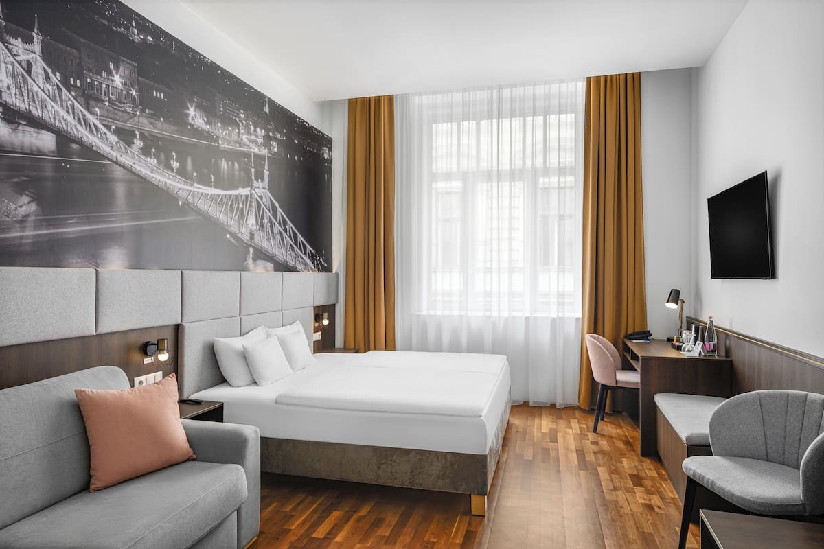 A hotel room with a large bed, a sofa, a desk, and a TV.