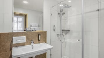 Un baño moderno con ducha envuelta en vidrio, un lavabo blanco y un espejo sobre él.