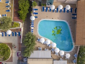 An aerial view of a hotel pool area with multiple lounge chairs and umbrellas, surrounded by trees and a tiled walkway. - Hotel Garda Bellevue (Limone sul Garda)
