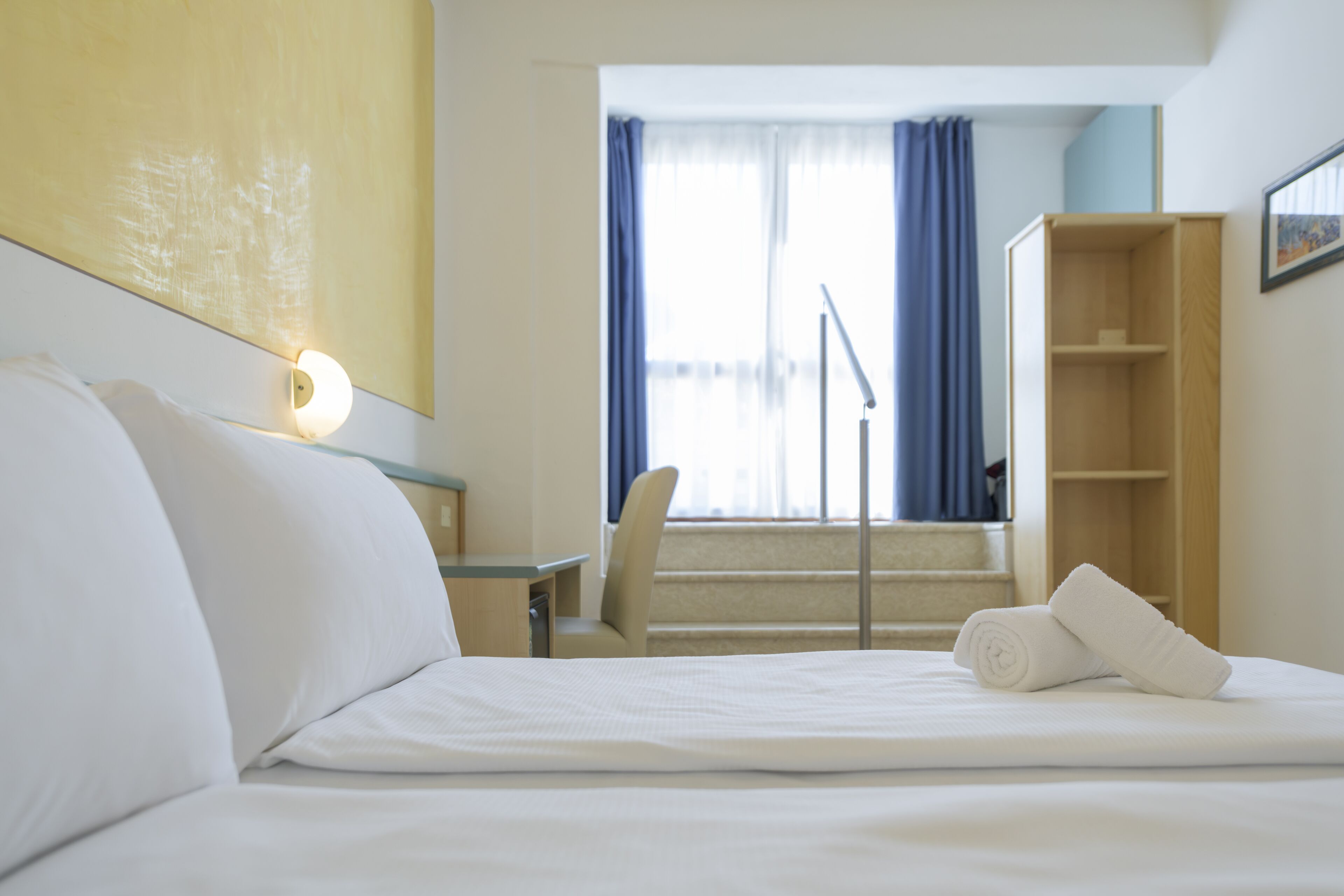 A hotel room with a bed, a desk, a chair, a staircase, and a wardrobe.