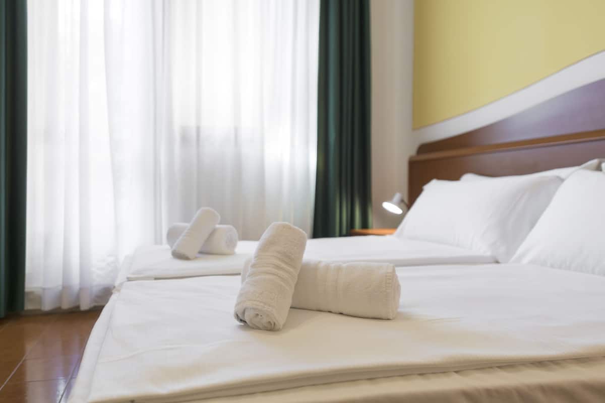 A hotel room with a neatly made bed, a pillow, and a rolled towel on the bed.