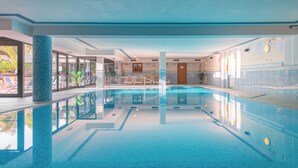 Piscina interna com água cristalina, rodeada por espreguiçadeiras e plantas em vasos.