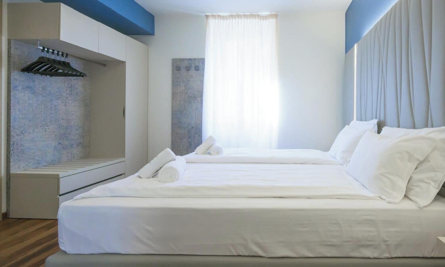 Una camera d'albergo moderna con un letto grande, un termosifone integrato e una finestra con tende.