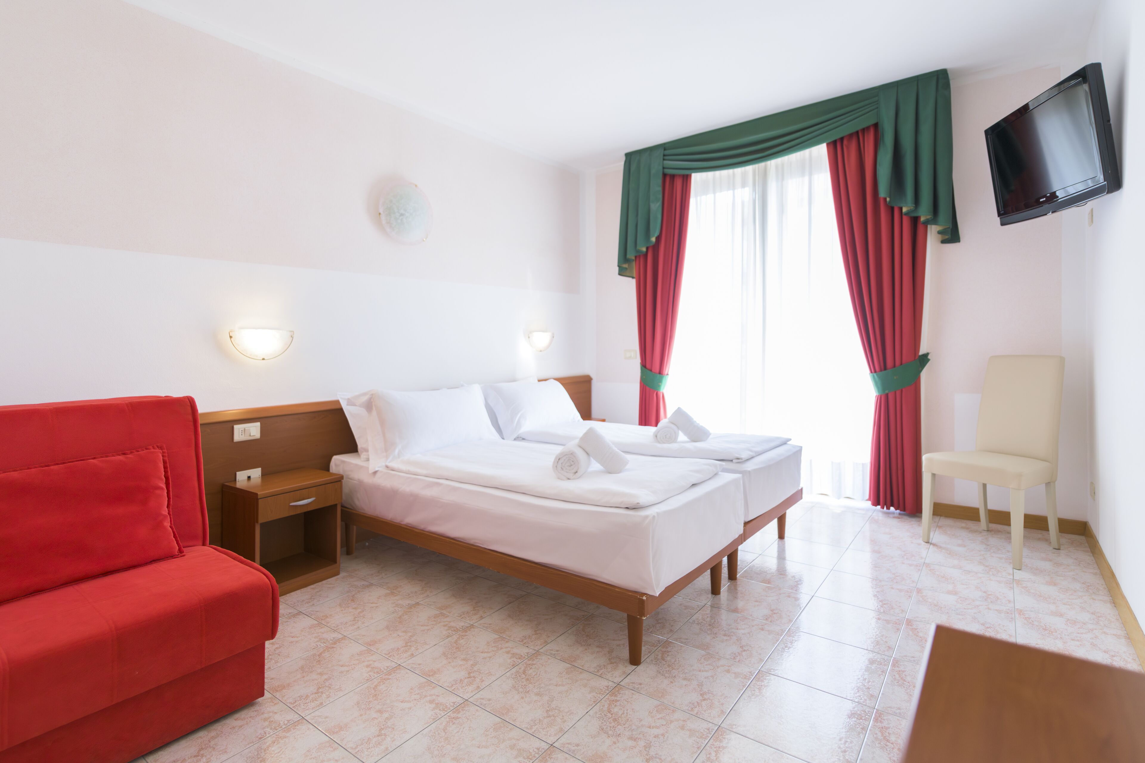 Une chambre d’hôtel avec un lit, un canapé rouge, une table de chevet en bois, une télévision et une chaise.