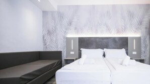 Quarto de hotel moderno com uma cama grande, um sofá cinzento e uma parede com padrão de folhas.