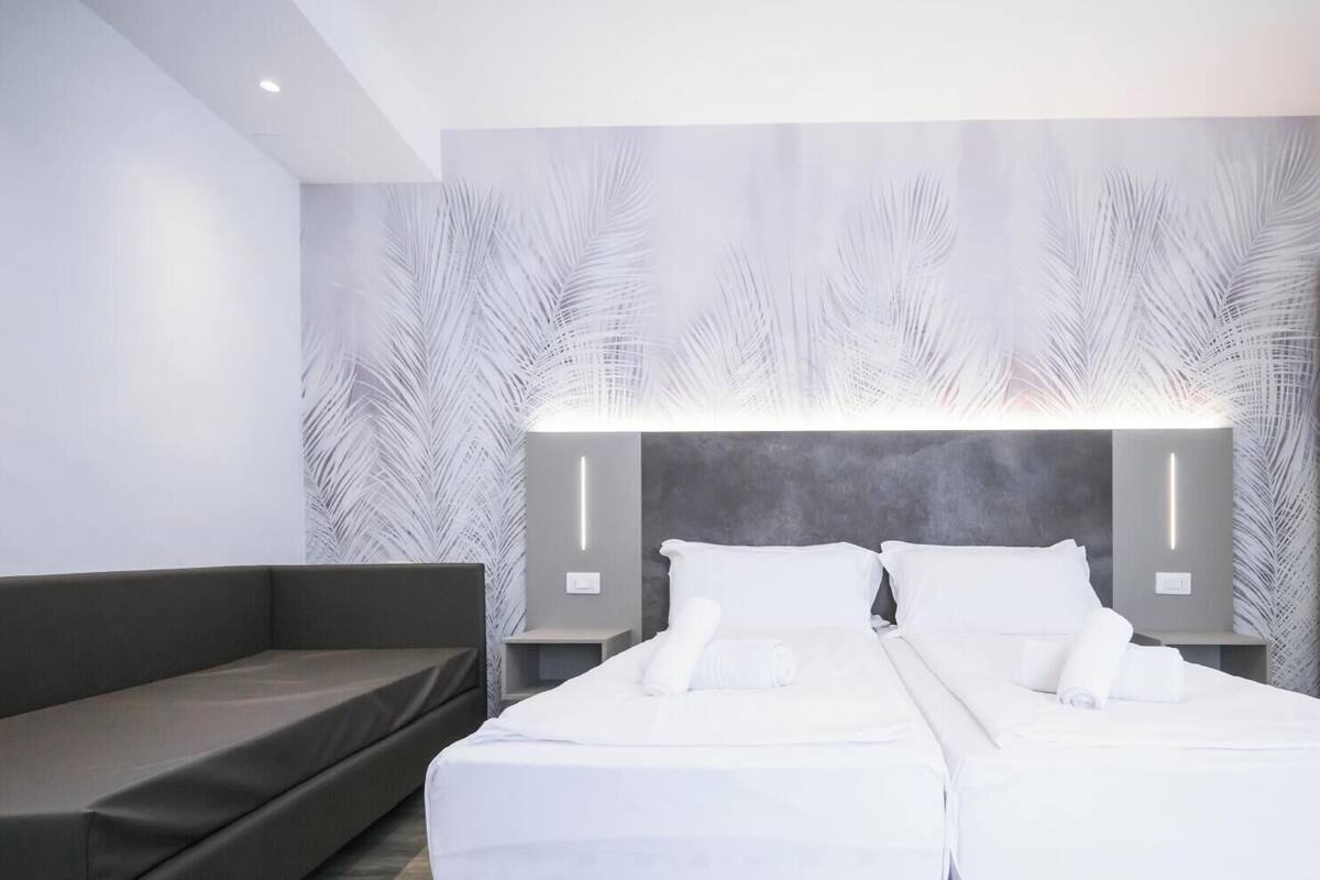 A modern hotel room with a large bed, a grey sofa, and a wall with a leaf pattern.
