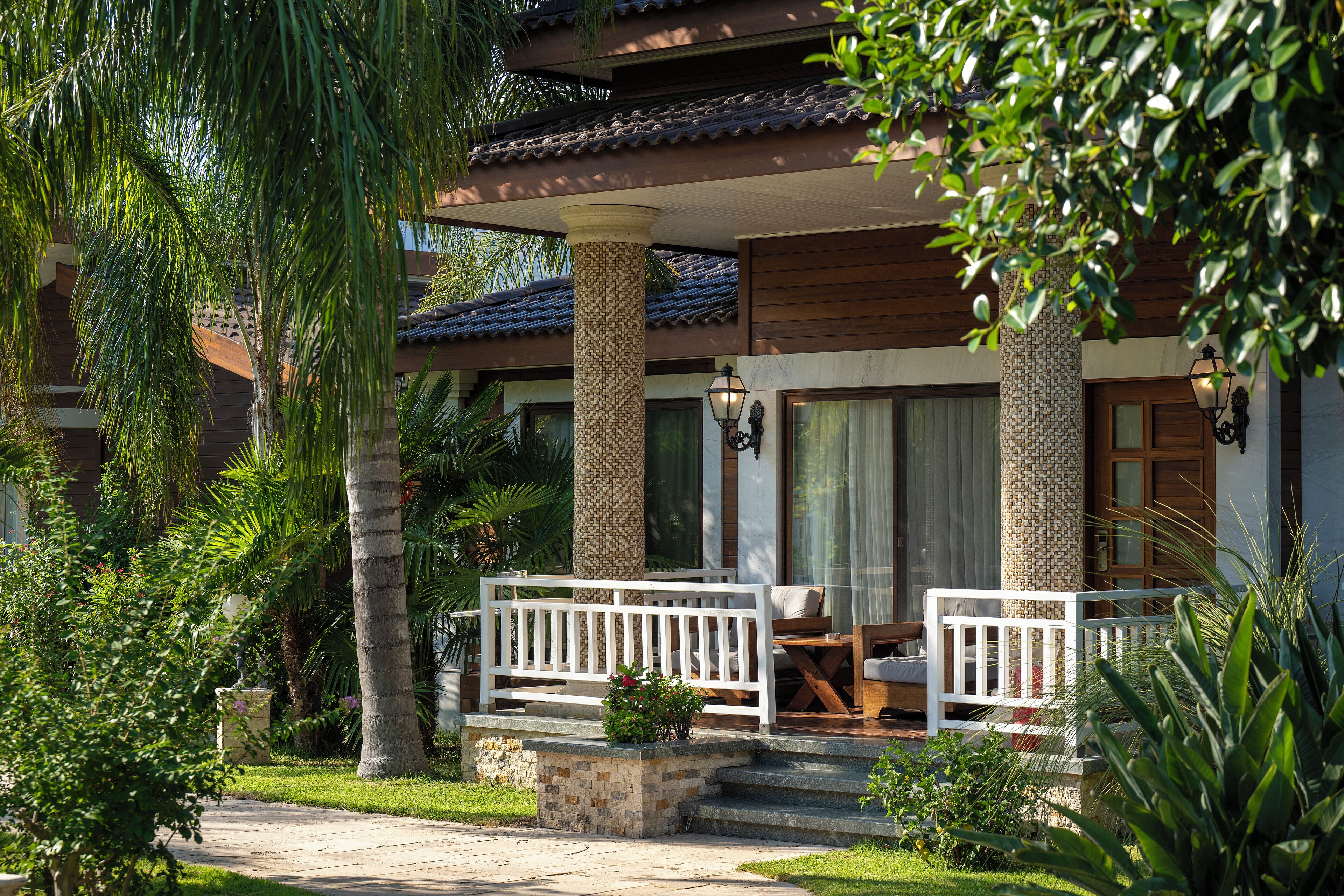 A covered outdoor seating area with a white railing, a stone planter with flowers, and a staircase leading to a wooden door.