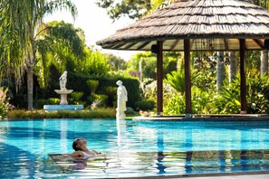 A swimming pool with a gazebo in the background, surrounded by lush greenery and statues.