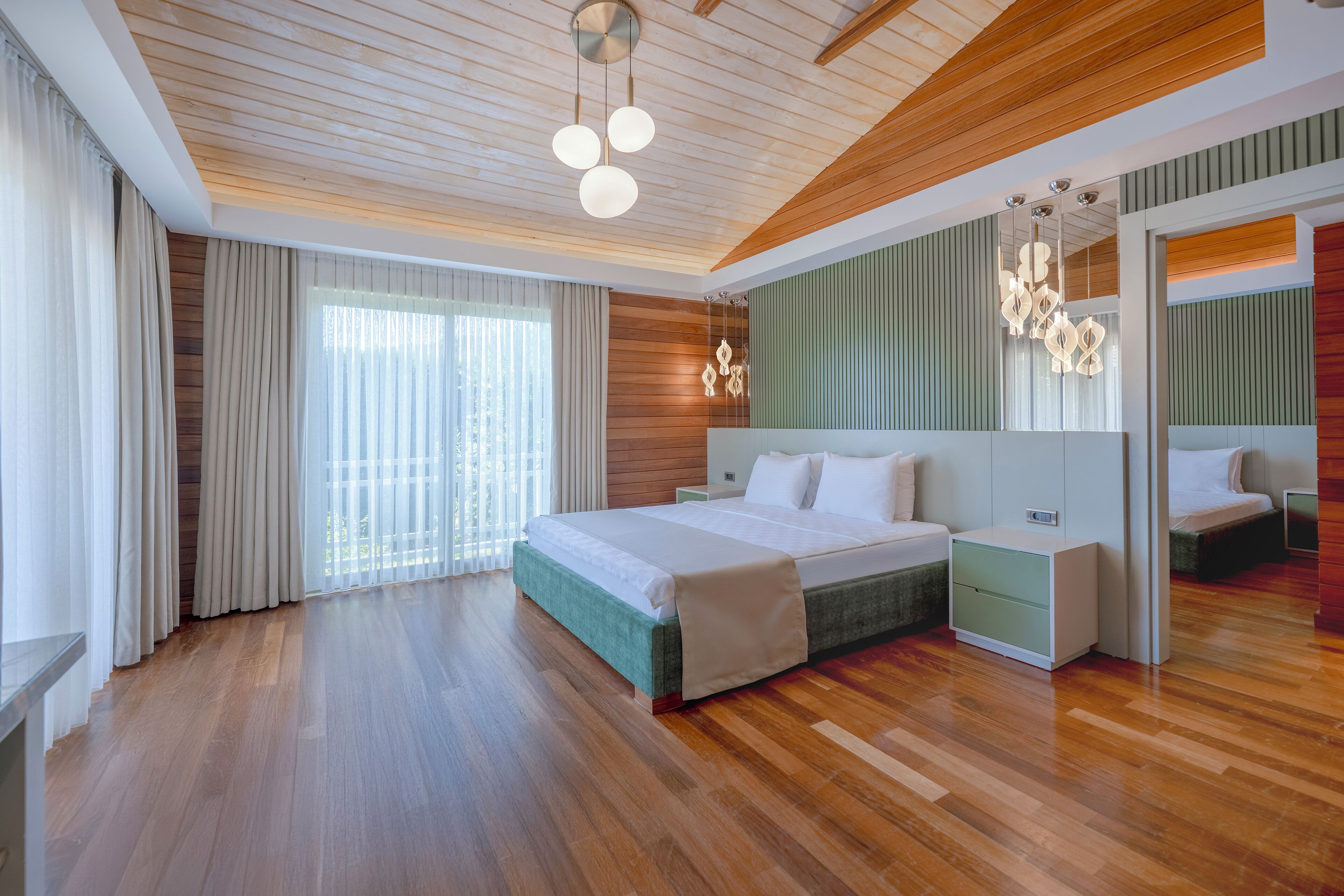A modern bedroom with a wooden ceiling, a large bed with white bedding, a nightstand, and a mirror.