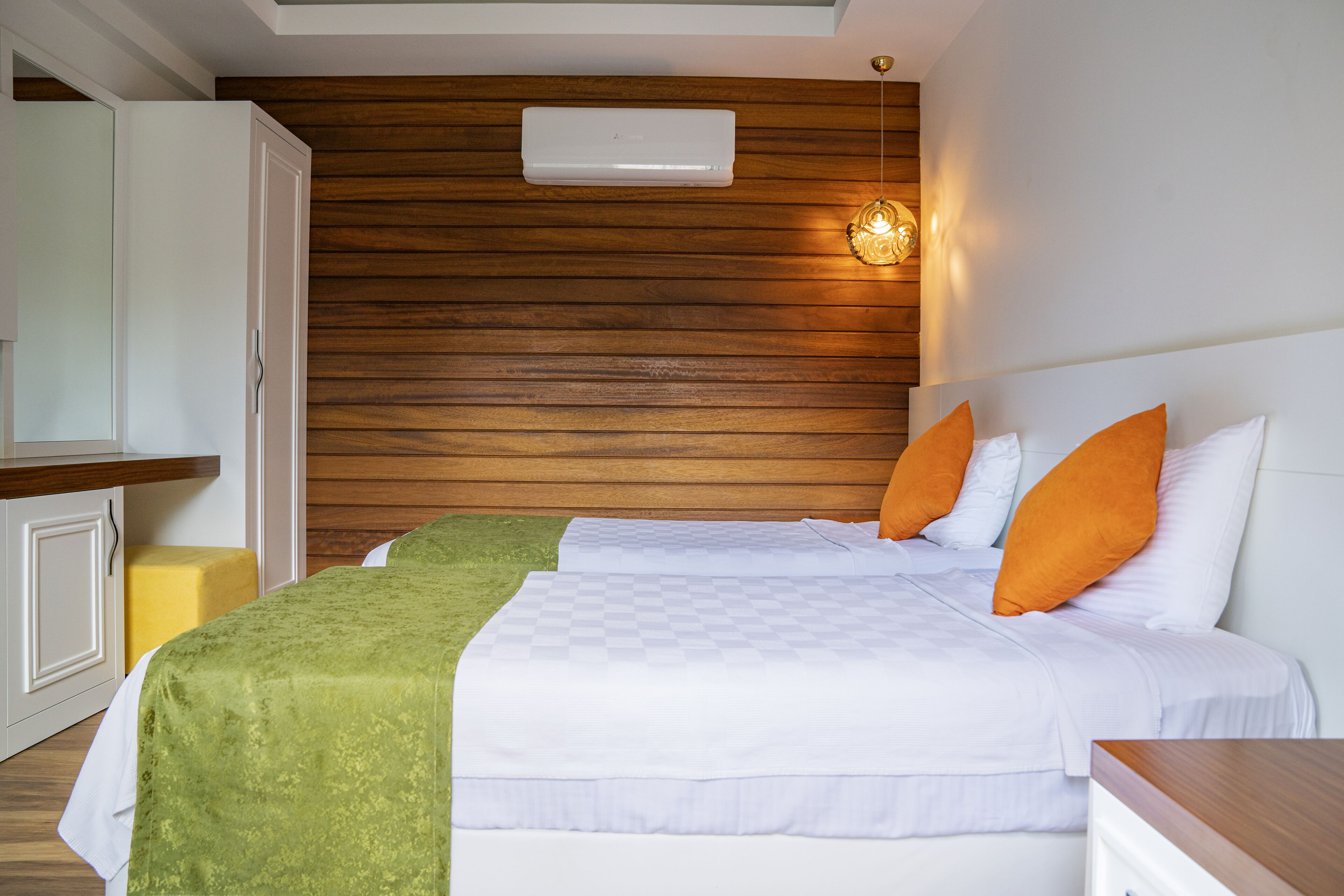 A hotel room with two beds, wooden paneling on the walls, a white air conditioning unit, and a small table.