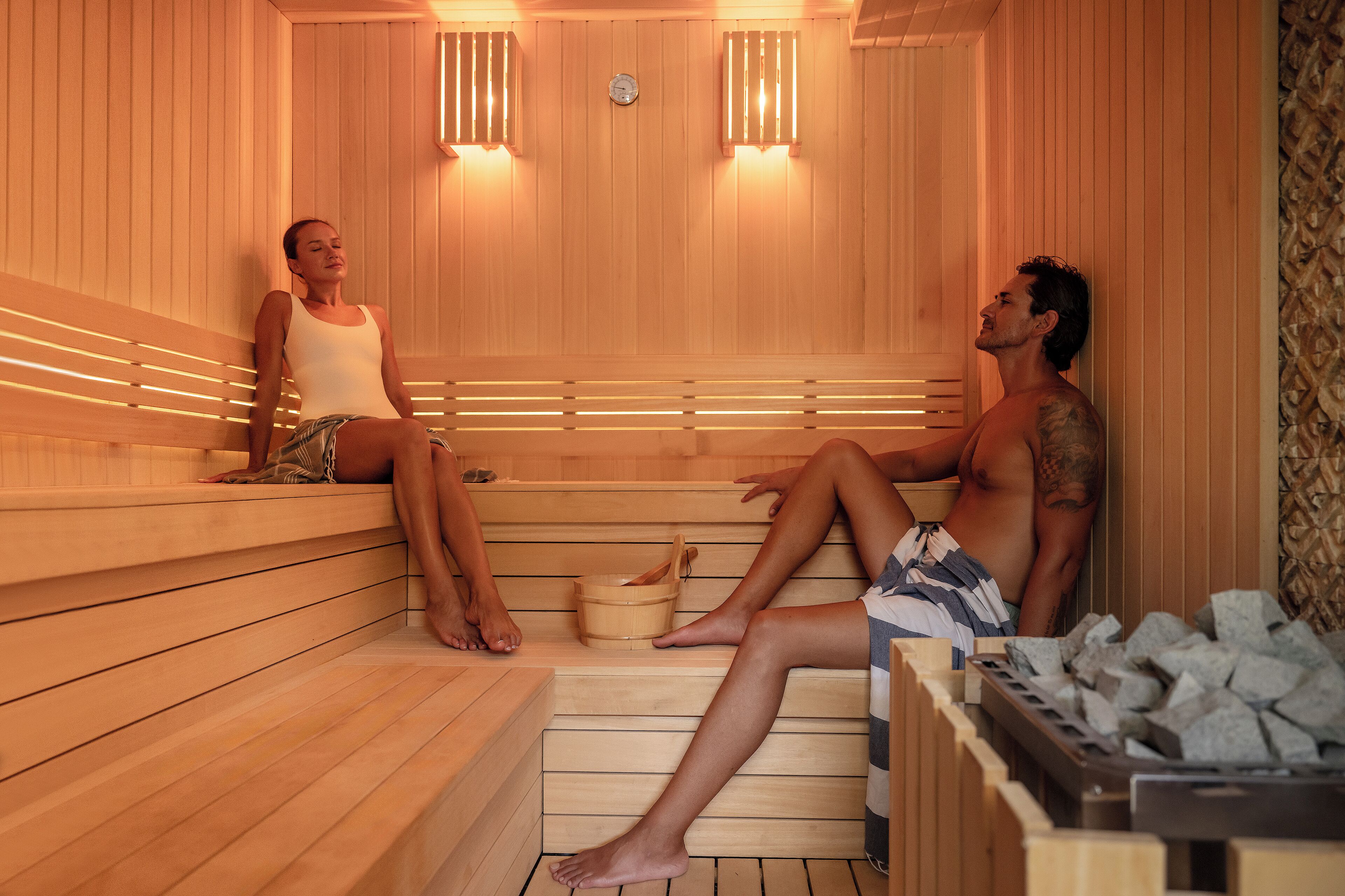 A sauna with wooden benches and benches, a wooden bucket, and a stone container.