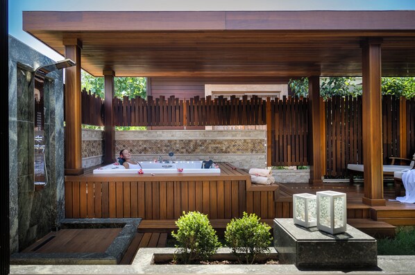Un área de spa con una bañera de hidromasaje, terraza de madera y macetas de piedra.