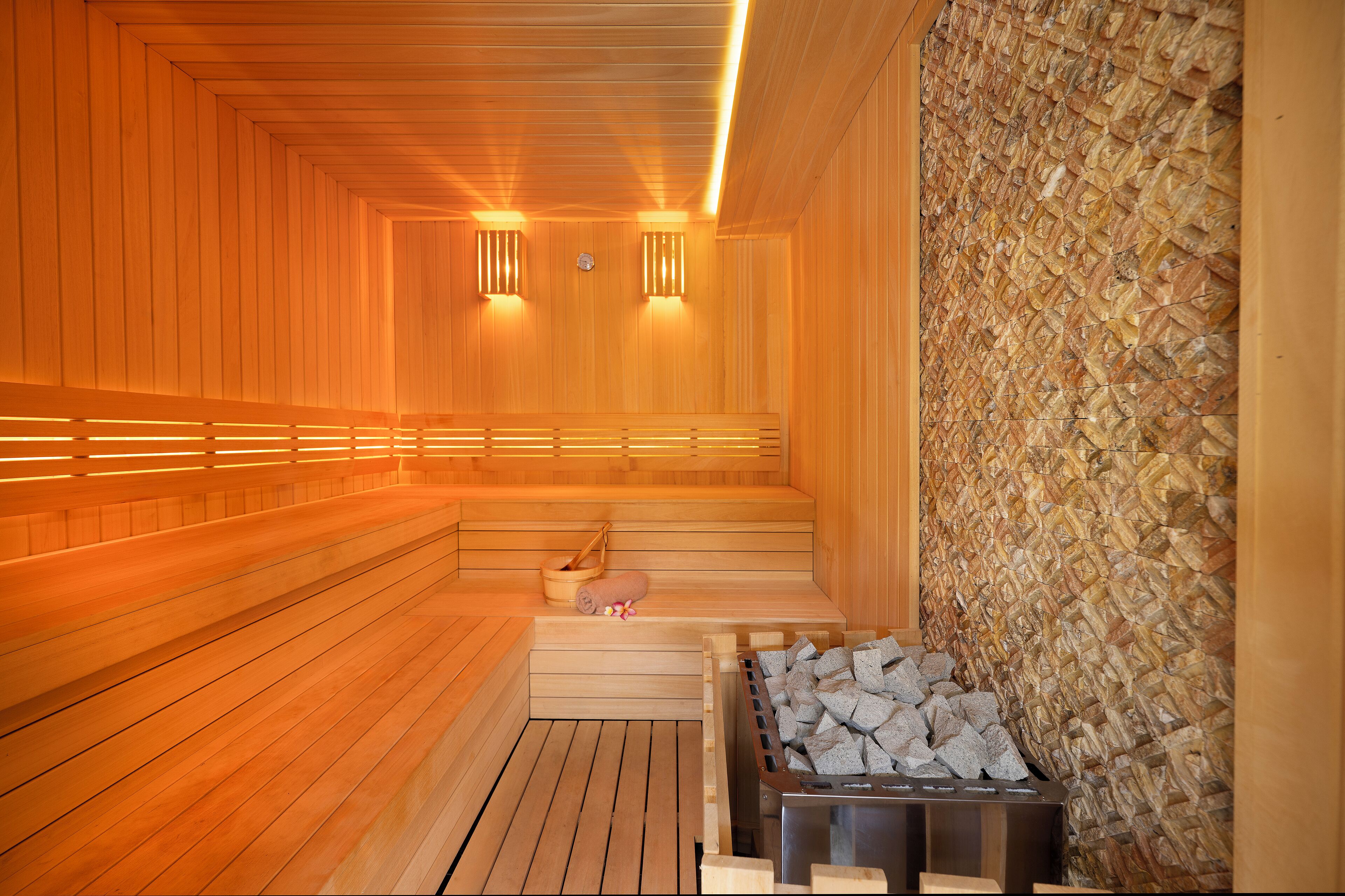 Una sauna amb bancs de fusta, paret de pedra i estufa de llenya.
