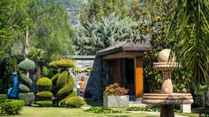 Un jardín bien cuidado con setos recortados, una estatua de Buda y un edificio de techo de paja.