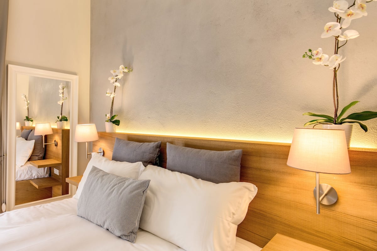 A neatly made bed with white and gray pillows, a wooden headboard, and two wall-mounted lamps.