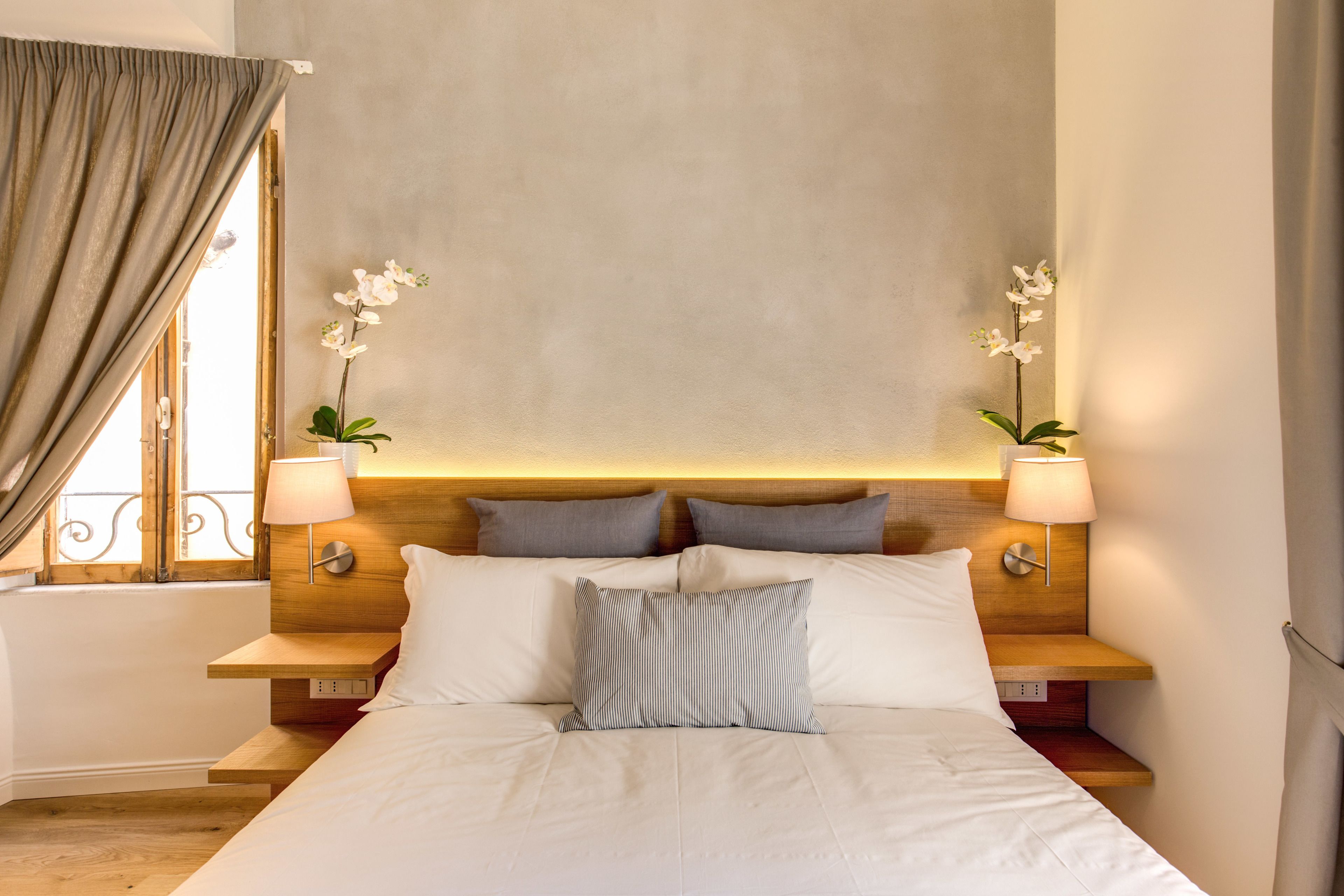 Un lit bien fait, avec des oreillers, une table de chevet avec une lampe et une plante orchidée.