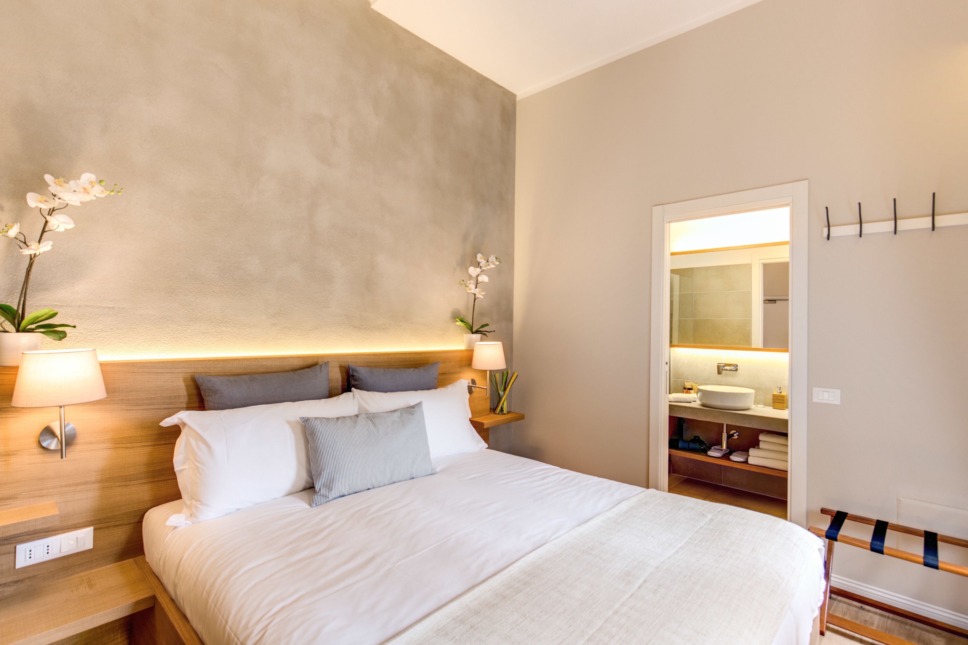 A modern hotel room with a large bed, bedside lamps, a nightstand, and a view into the bathroom.
