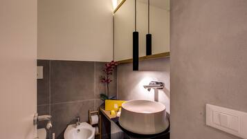 A modern bathroom with a large vessel sink, a bidet, and a mirror with pendant lights.