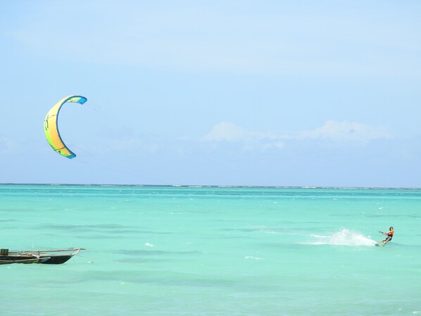 A person windsurfing in turquoise waters with a boat in the foreground.
