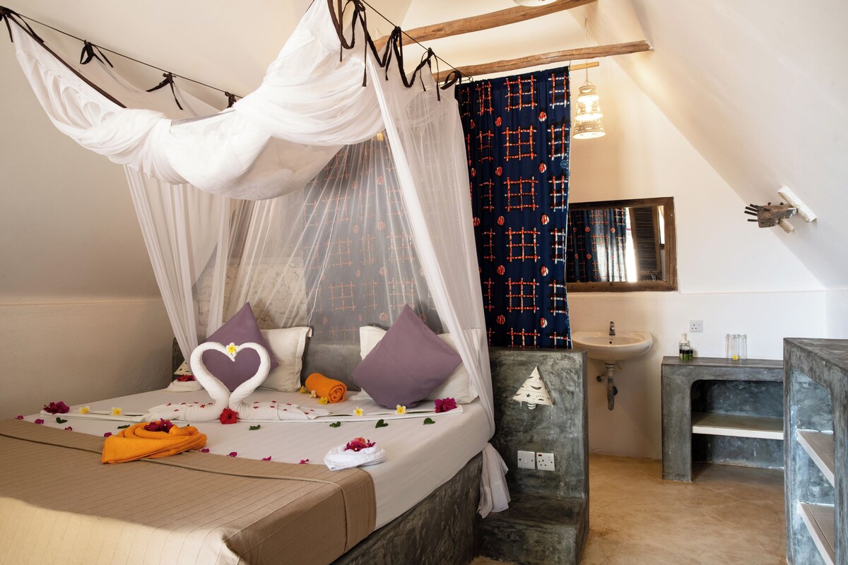 Une chambre à coucher avec un lit à baldaquin, une table de chevet avec une serviette, une commode, une petite table de chevet, une étagère murale, un miroir et une salle de bain avec un lavabo et un porte-serviettes.