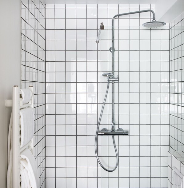 Une douche moderne dotée d’un pommeau de douche à main et d’une grande pomme de douche fixée au plafond, le tout installé sur un mur carrelé.