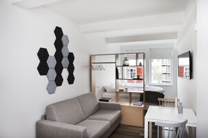Una habitación moderna y minimalista con un sofá gris, una mesa blanca y una pieza de arte mural hexagonal.