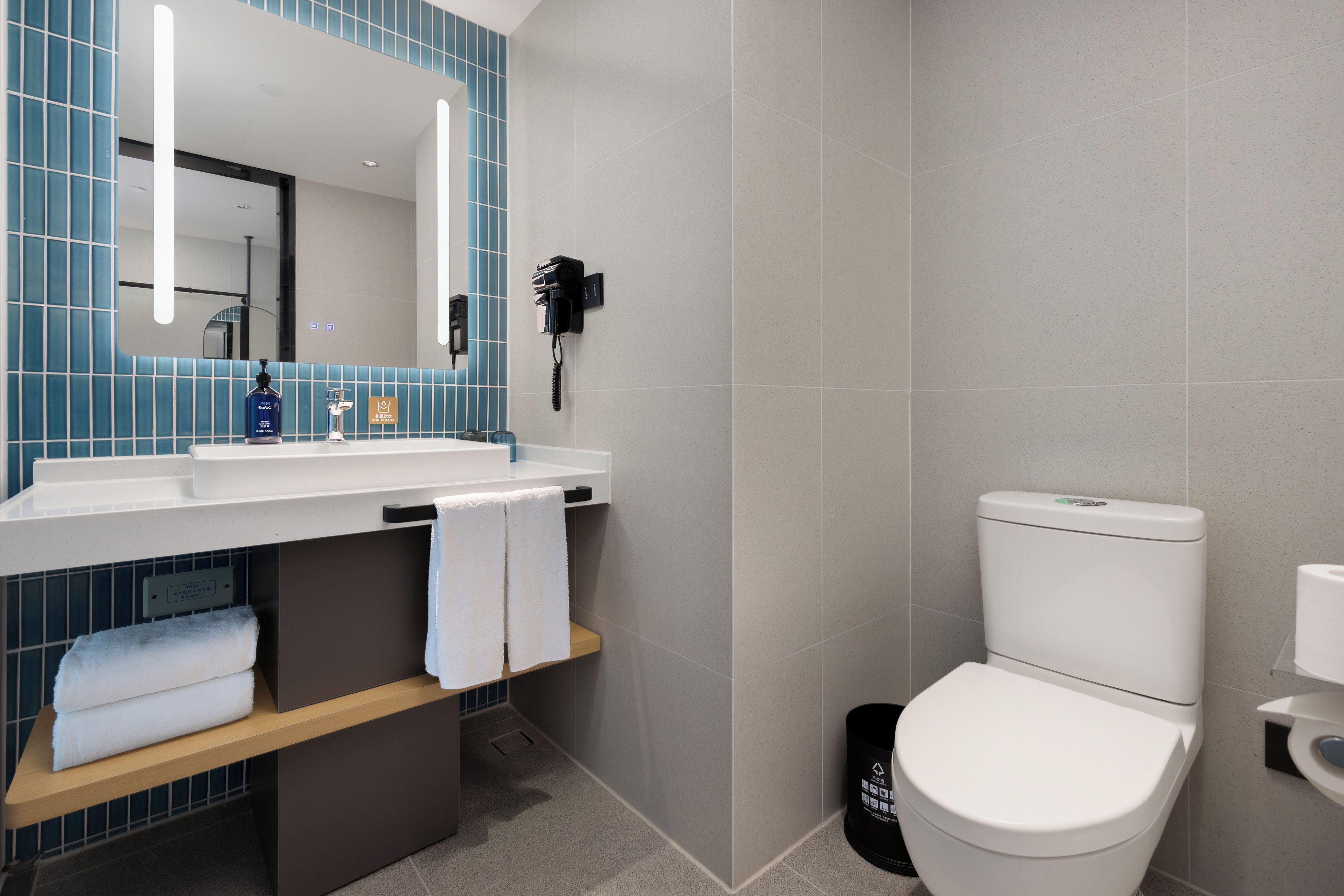 A modern bathroom with a white sink, a mirror, a hairdryer mounted on the wall, and a toilet.