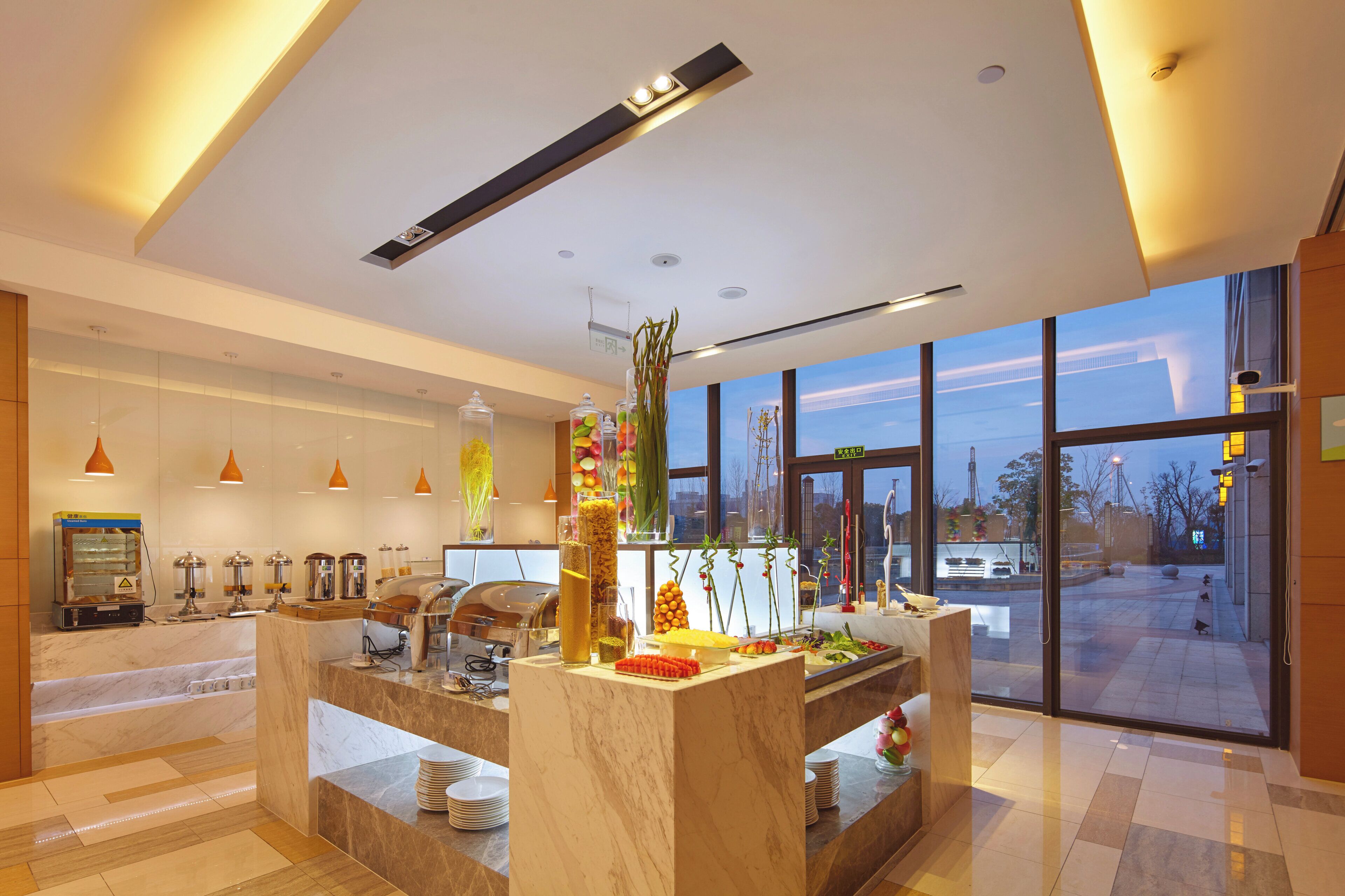 A modern hotel lobby with a reception desk, seating area, and large windows offering a view of the outside.