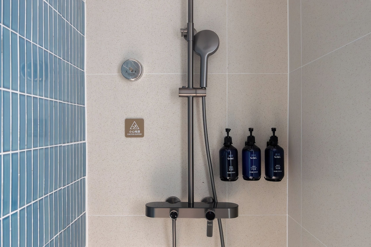 A modern shower with a rain shower head, handheld showerhead, and a handheld soap dispenser.