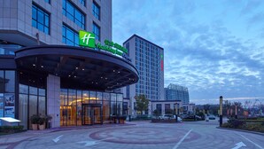 A hotel entrance with a large glass facade, a curved roof, and a prominent green 'f' logo. - Holiday Inn Express Shanghai Jiading Industry Park by IHG (Shanghai)