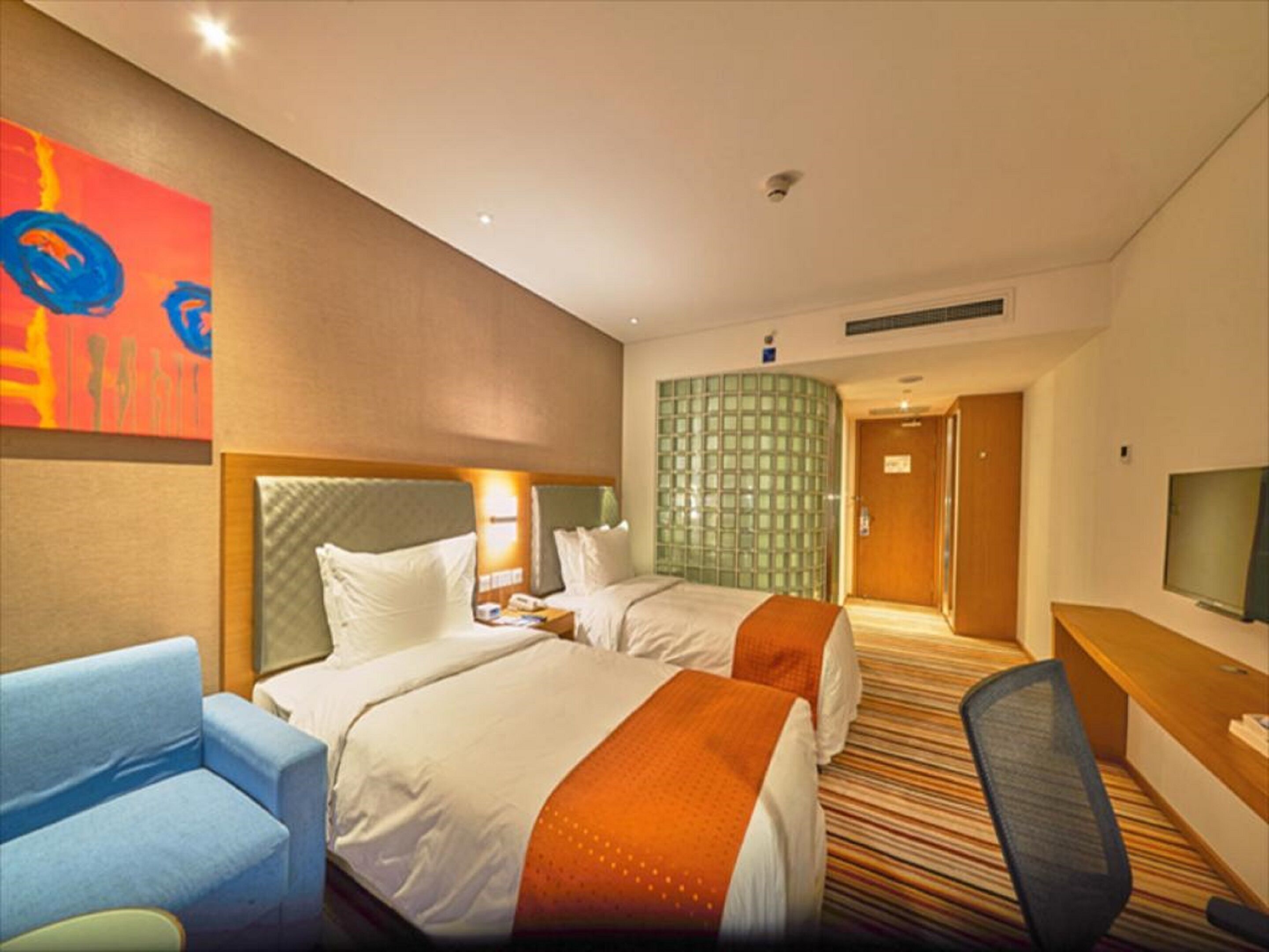 A hotel room with two beds, a desk, a chair, a television, and a colorful abstract painting on the wall.