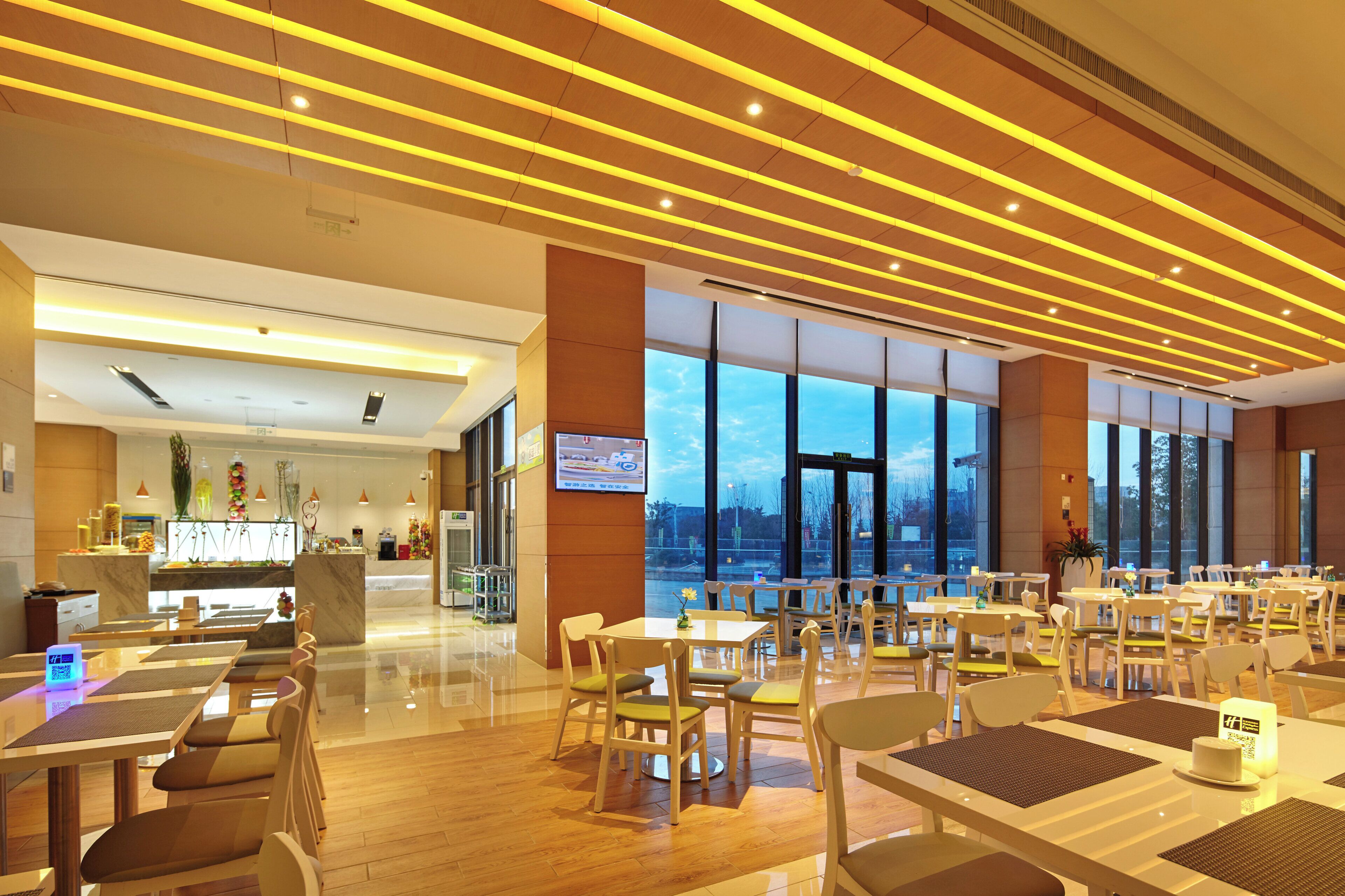 Un restaurant spacieux au design moderne, doté d’un bar et de grandes fenêtres offrant une vue sur le paysage urbain.