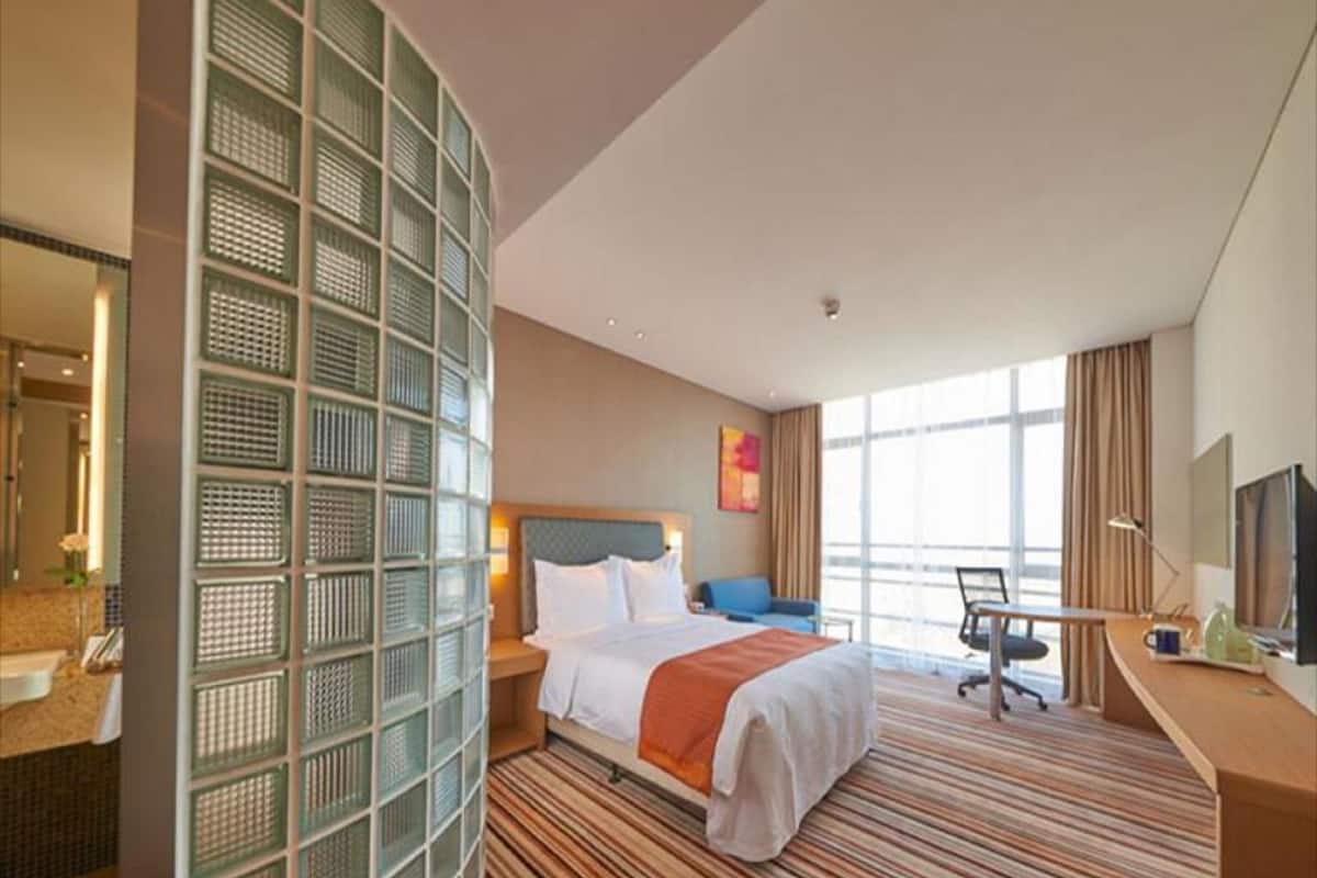 A hotel room with a bed, a desk, a chair, a TV, and a large window.