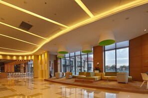Eine geräumige Lobby mit modernem Design, ausgestattet mit einer zentralen Sitzecke, Sofas und Sesseln, einem großen Fenster mit Blick hinaus und einer Decke mit eingelassener Beleuchtung.