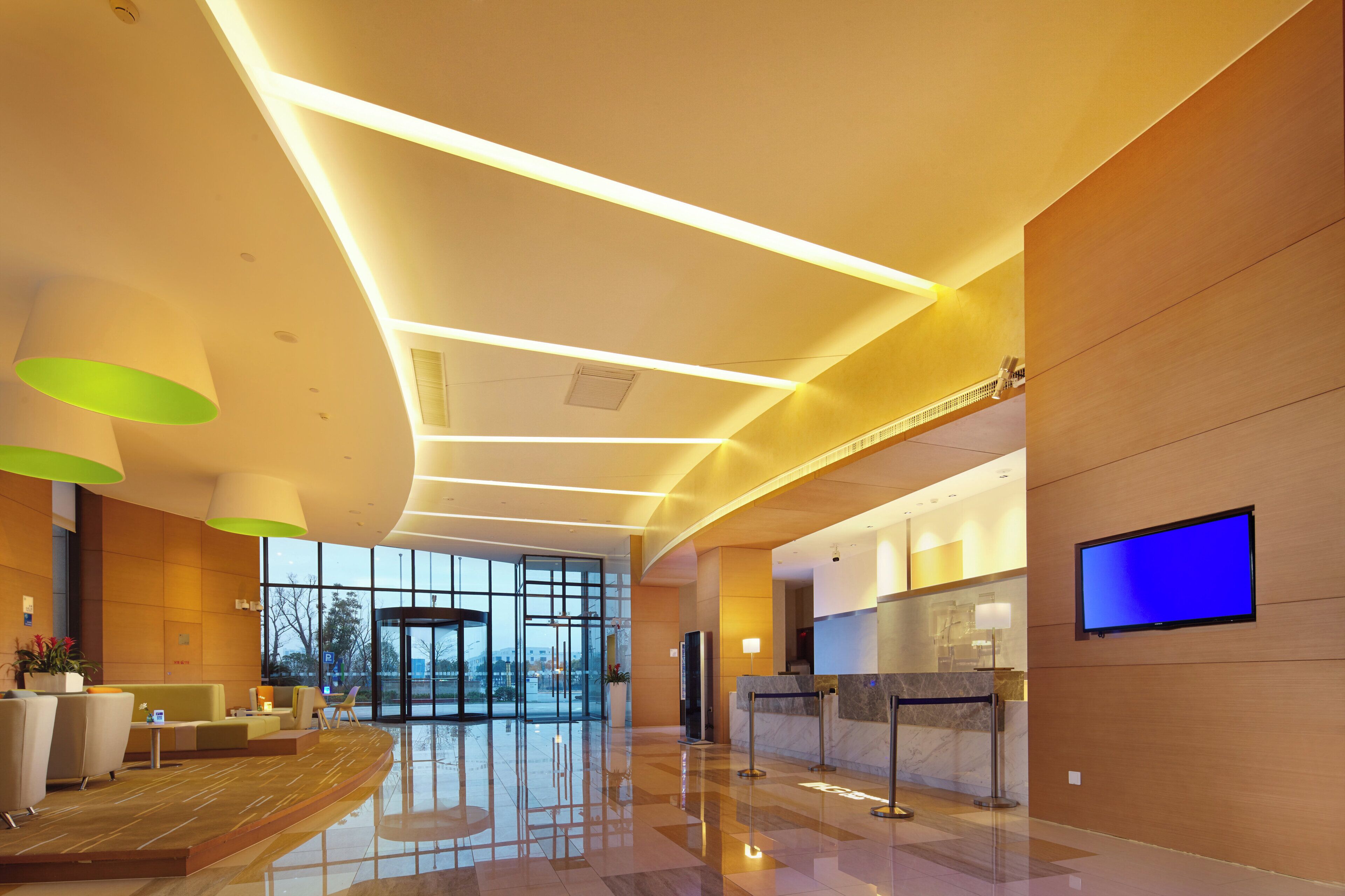 A modern hotel lobby with a reception desk, seating area, and large windows.